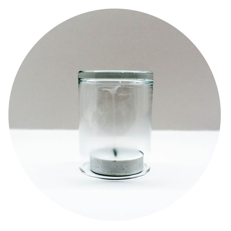 Photo of a tea light covered by a clear glass with smoke inside.