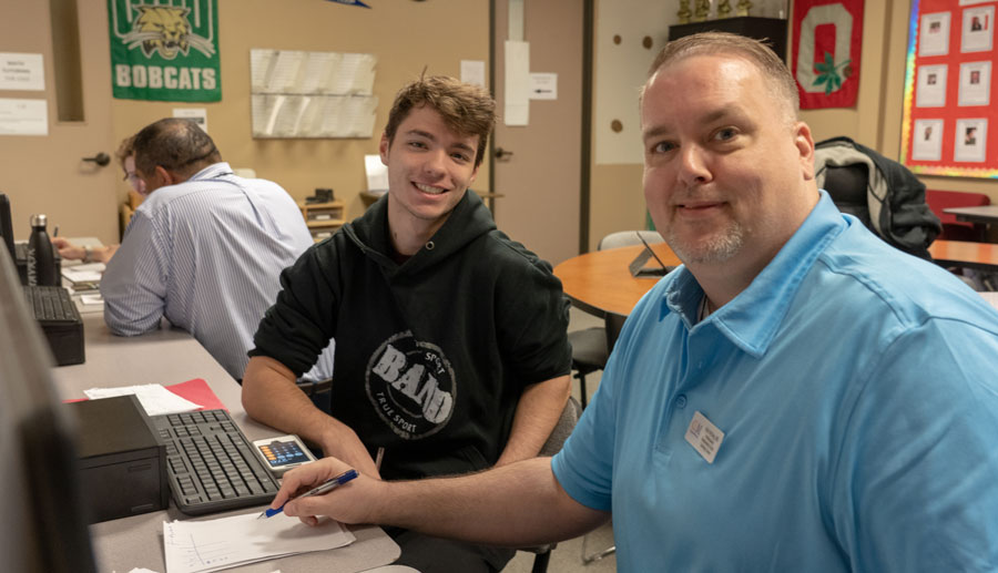 Young man sitting with a math tutor smiling at the camera