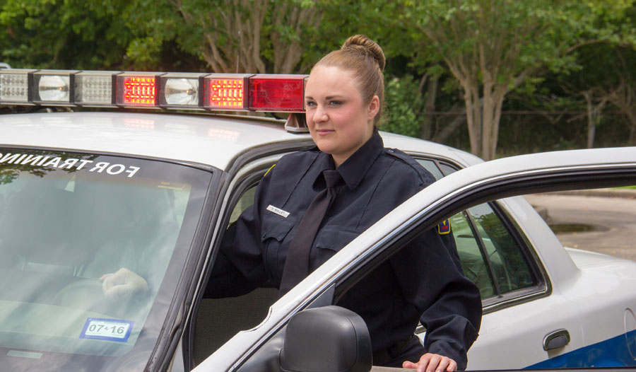 Female criminal justice student standing outside of police car